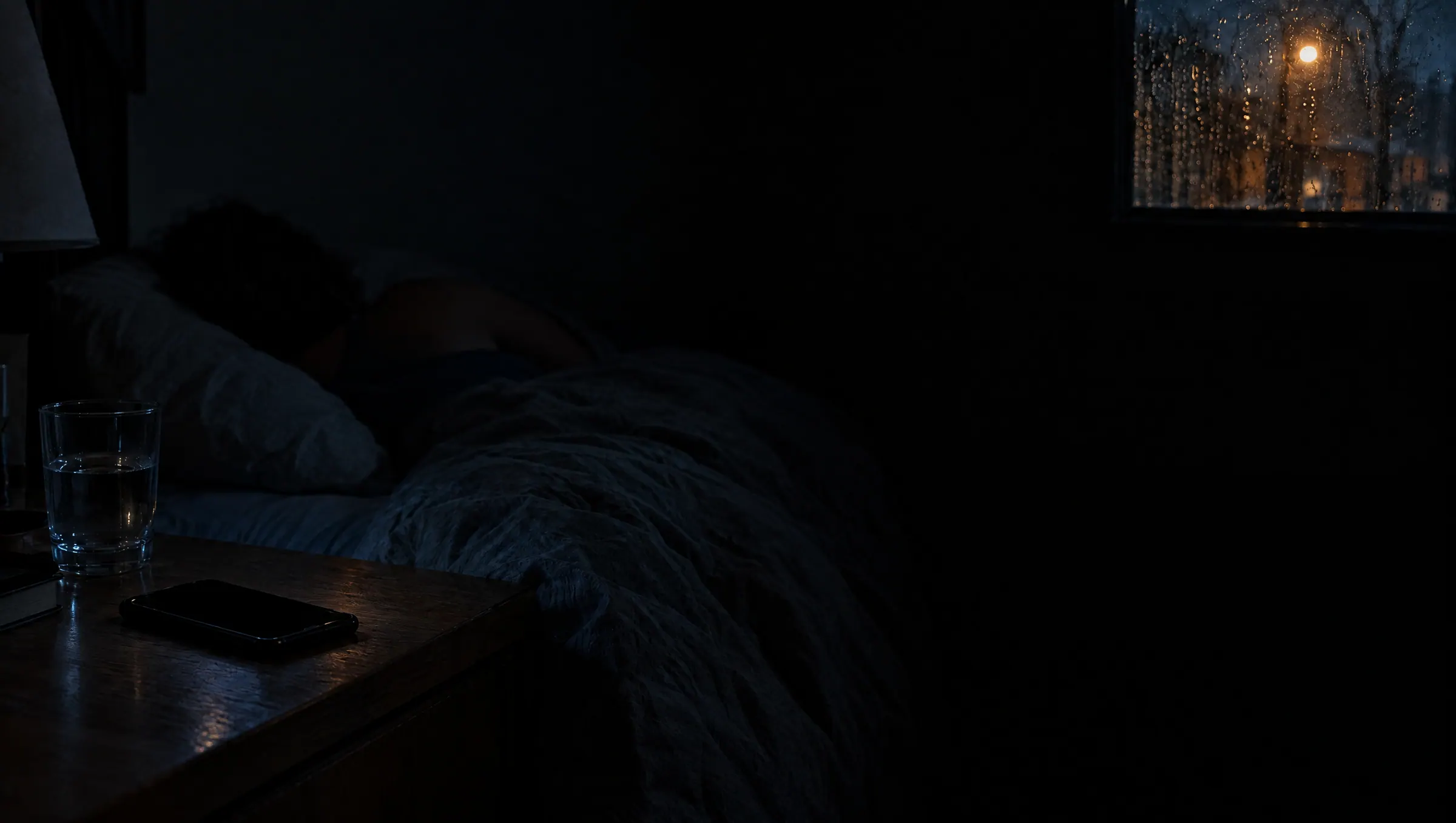 A dark bedroom at 2:14 AM, someone asleep, a phone face up on the nightstand
